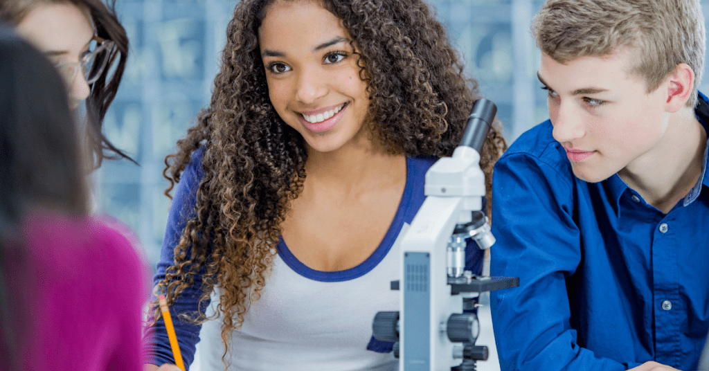 high school student sitting in front of a microscope